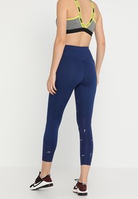Leggings bleu marine avec une taille haute et un tissu qui évacue l'humidité. Présentent des motifs en forme de virgule blancs et une texture lisse et extensible.
