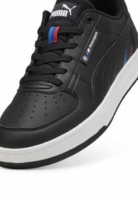 Fekete bőr sneaker, texturált felülettel, fehér talppal, fekete fűzőkkel és színes csíkokkal. A BMW logo és a Puma márkajelzés díszíti.