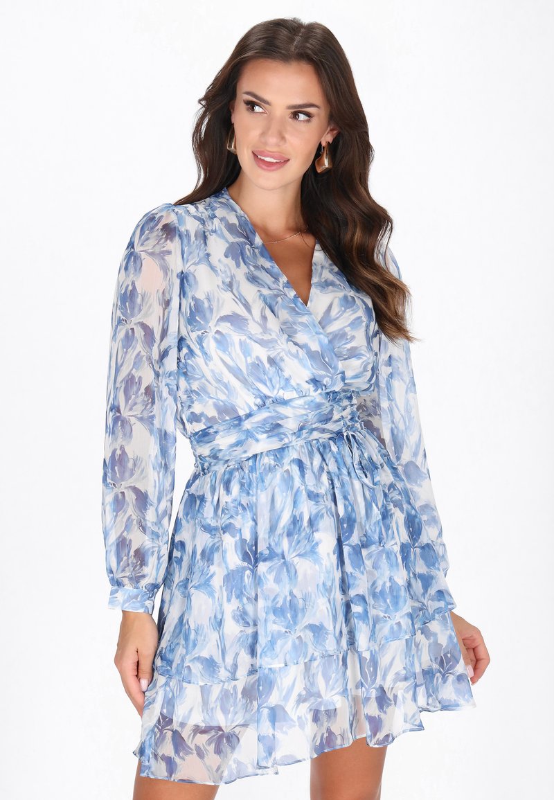 Vestido floral azul hecho de tejido ligero, con un diseño envolvente, mangas largas, volantes en capas y un detalle de cinta en la cintura.