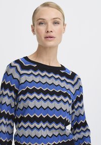Stickad tröja med ett zigzag-mönster i blått, grått och svart. Rundad halsringning, ribbade ärmmuddar och texturerad tyg.