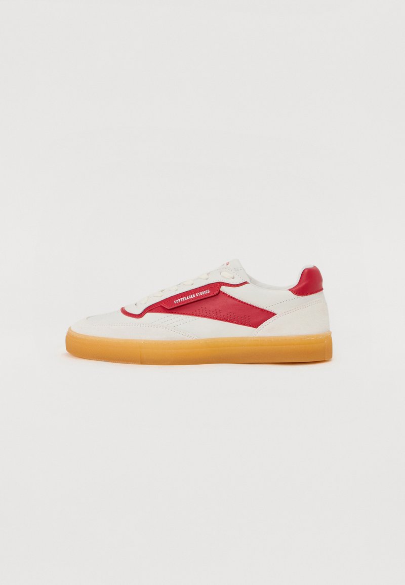 Vit och röd sneaker med gummisula, som har ett glansigt läderöverdrag, texturerade detaljer och en logotyp på sidan.