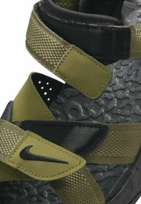Sandale negre și verzi măslinii, cu curele ajustabile, talpă texturată și logo Nike. Materialele includ plasă și partea superioară sintetică.