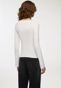 Top bianco a maniche lunghe con scollatura rotonda, caratterizzato da una silhouette aderente e una texture morbida, abbinato a jeans neri a vita alta.