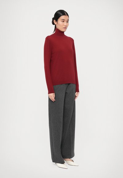 Rød genser med høy krage og lange ermer, kombinert med grå vidt skjørtbukser. Antrekket har en jevn tekstur og minimalistisk design.