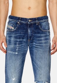 Jeans i blekt blå denim med slitna detaljer, fem fickor, knapplåsning och dragkedja samt sömnadseffekter på midjebandet.