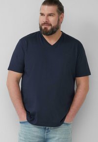 Navyblauwe t-shirt met korte mouwen en V-hals, gemaakt van zachte stof, met een relaxte pasvorm en minimale branding op de borst. Draagt met lichtblauwe jeans.