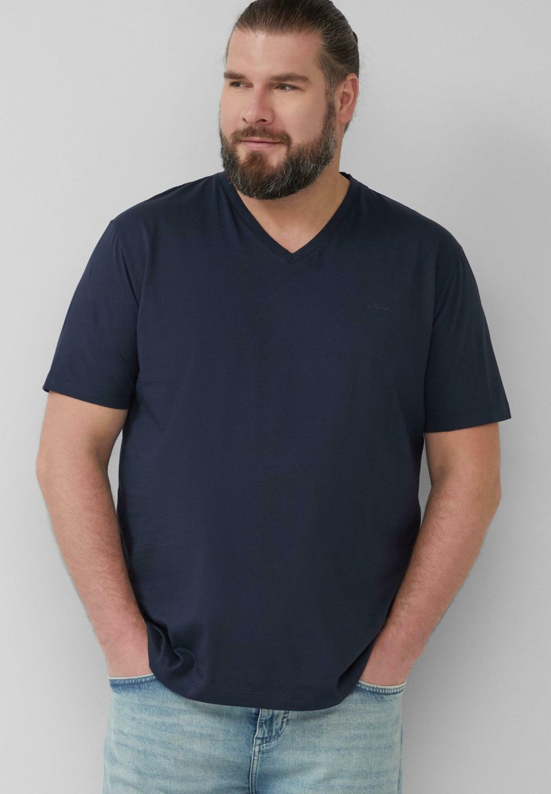 Navyblauwe t-shirt met korte mouwen en V-hals, gemaakt van zachte stof, met een relaxte pasvorm en minimale branding op de borst. Draagt met lichtblauwe jeans.