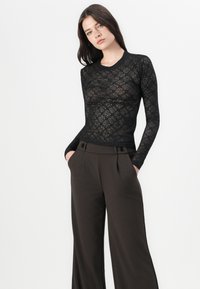 Haut en dentelle noire à manches longues avec un motif floral, associé à un pantalon large marron taille haute avec des plis avant et des accents de boutons.