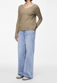 Pull en maille côtelée beige avec un col en V, associé à un jean large bleu clair. Le pull a des manches longues et une coupe décontractée.