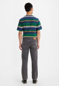 Camiseta de algodón a rayas con líneas verdes, marinas y naranjas; combinada con jeans de mezclilla gris oscuro que tienen bolsillos traseros y una etiqueta de cuero.