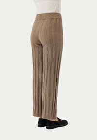 Beige, gerippte Strickhose mit hohem Bund, weit geschnitten und aus strukturiertem Stoff. Getragen mit dunklen Slippern.