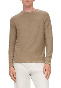 Langarm beige shirt met een ronde hals, gemaakt van een gestructureerde stof; zichtbare stiksels langs de zoom en manchetten; gedragen met witte broek.