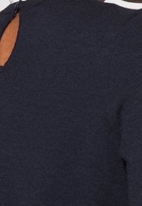 Marinblå stickad topp med en texturerad väv, ett V-format ryggutskärning och en liten knappstängning vid nacken.