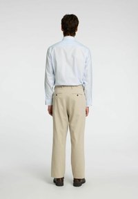 Camicia azzurro chiaro a maniche lunghe con polsini a bottoni, abbinata a pantaloni a quadri beige con due tasche posteriori e scarpe marroni.