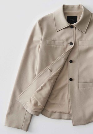 Beige maßgeschneiderte Jacke mit Kragen, zwei Fronttaschen und schwarzen Knöpfen. Innenfutter aus glattem Stoff. Einfaches, minimalistisches Design.