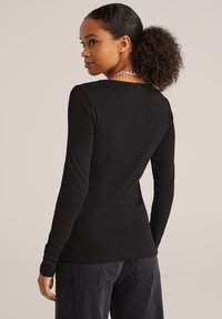 Top de manga larga negro de canalé con escote en forma de barco y diseño ajustado, combinado con pantalones vaqueros oscuros de cintura alta.