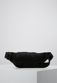 Black fabric fanny pack with a rectangular shape, adjustable strap, and a smooth texture. Features a large zipper pocket for storage.