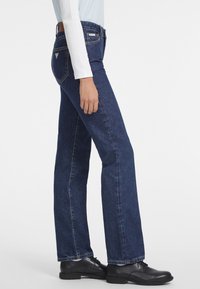 Vaqueros de mezclilla azul oscuro de pierna recta con una cintura de altura media, que presentan un diseño clásico de cinco bolsillos y sutiles acentos de marca.