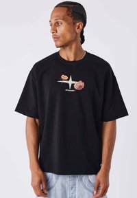 Camiseta de algodón negra con un gráfico floral y un diseño de estrellas en el centro. Corte holgado con un cuello redondo y mangas cortas.