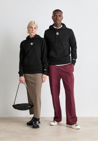Black hoodies with front pockets, paired with a brown skirt and burgundy trousers. Footwear includes black sneakers and cream shoes.