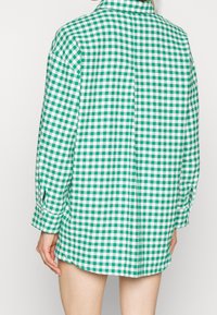 Green and white checkered shirt with long sleeves, a collar, and button details at the cuffs. The fabric has a smooth texture.