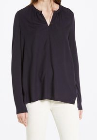 Blusa a maniche lunghe di un blu navy scuro, caratterizzata da una vestibilità rilassata, scollatura a V con dettaglio arricciato e un orlo posteriore leggermente più lungo. Realizzata in tessuto leggero.