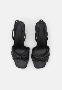 Musta korolliset sandaalit neliömäisellä kärjellä, joissa on solmittujen hihnojen muotoilu ja ohuet nilkkahihnat pehmeästä nahkamateriaalista.