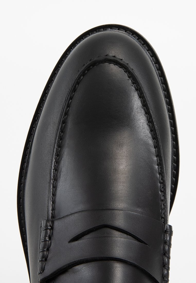 Zwarte leren instappers hebben een gladde textuur met decoratieve stiksels en een schuine band over de wreef. Klassiek puntige neus ontwerp.
