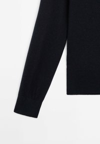 Musta neulepaita, jonka hihassa on ribattu resori. Se on sileäpintainen ja suora malli, ilman lisäkuvioita tai koristeita.