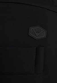 Svarta träningsleggings med en texturerad lapp med hexagonalt mönster och subtil logotyp. Slät tyg med elastisk midjeband.