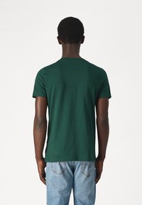 T-shirt in cotone verde con collo rotondo e maniche corte, caratterizzato da una texture liscia e una vestibilità comoda. Indossato con jeans azzurri chiari.