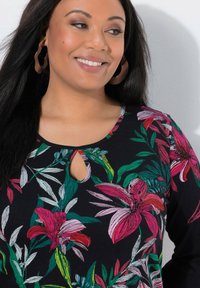 Czarna bluzka z długim rękawem ozdobiona kwiatowym wzorem z różowymi liliami i zielonymi liśćmi. Okrągły dekolt z wycięciem na klatce piersiowej.
