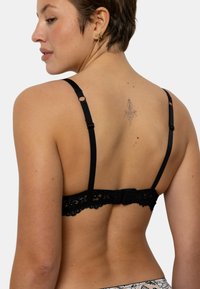 Soutien-gorge en dentelle noire avec bretelles ajustables, doté d'une fermeture à crochets et œillets au dos et de délicats détails en dentelle le long de la bande.