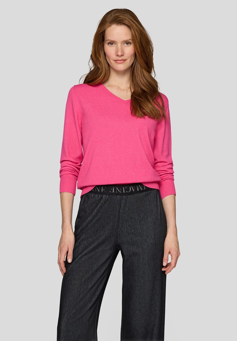 Knallpinkes V-Ausschnitt-Pullover mit langen Ärmeln, kombiniert mit locker sitzenden, dunkel gestreiften Hosen mit elastischem Bund und Logodetail.
