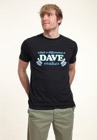 Camiseta de algodón negra con texto azul que dice "qué diferencia hace un DAVE", con un gráfico de un pulgar hacia arriba. Diseño ajustado, mangas cortas.
