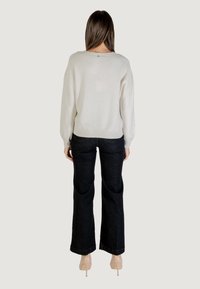 Pull beige clair avec un tricot texturé et un léger éclat, associé à un jean évasé sombre. Le pull a une coupe décontractée et un ourlet côtelé.