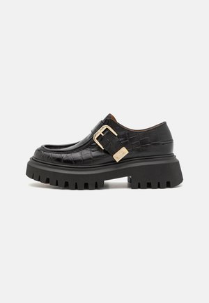 Black leather shoes with a crocodile texture, featuring a gold buckle accent, chunky black platform sole with deep grooves, and rounded toe design.