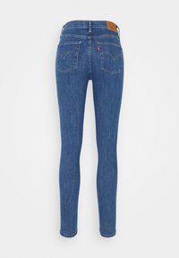 Smal jeans i blå denim med bakfickor, en brun läderetikett vid midjan och sydda detaljer på fickorna.