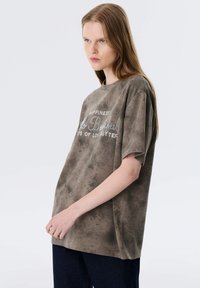 Oversized taupe t-shirt van zachte stof, met een gestructureerd oppervlak en metallic letters op de voorkant. Casual, losse pasvorm.