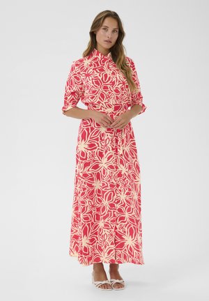 Maxikleid im rosa und cremefarbenen Blumenmuster, mit hohem Kragen, kurzen Ärmeln, tailliertem Bund und fließendem Stoff. Weiße High Heels runden den Look ab.