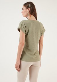 Olive green short-sleeve top with a textured fabric, casual fit, round neckline, and small rolled sleeves, paired with beige leggings.