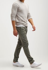 Jasnoszara sweter w paski, oliwkowe zwężane spodnie i białe trampki z czerwonymi akcentami. Casualowy strój o teksturowanym splocie.