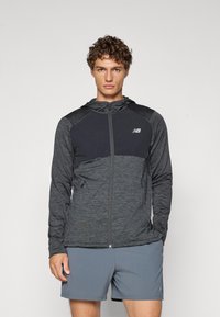 Haut à capuche zippé noir et gris avec un tissu texturé, un design ajusté et des poches latérales. Présente un logo sur la poitrine et une capuche.
