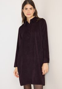 Dlouhé rukávy, bordó kordové šaty s límečkem a detailním zapínáním na knoflíky. Tkanina má jemnou texturu a decentní proužkovaný vzor.
