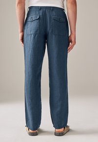 Pantaloni in lino blu scuro con vestibilità rilassata, dotati di due tasche posteriori e finitura semplice. La texture sembra leggermente stropicciata e morbida.