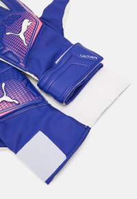 PUMA keepershandschoenen in het blauw met een getextureerde latex palm, versterkte vingergebieden en een klittenbandsluiting voor een veilige pasvorm. Voorzien van roze accenten.