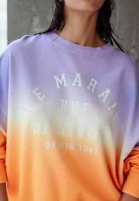Lila és narancs színátmenetes pulóver, fehér felirattal: "LE MARAIS RUE DE RIVOLI DEPUIS 1987." Puha pamut anyag, laza szabású.