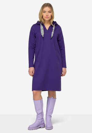 Paarse hoodie jurk met lange mouwen, voorzien van een V-hals en twee voorzakken. Gecombineerd met kniehoge lavendel rubberen laarzen.