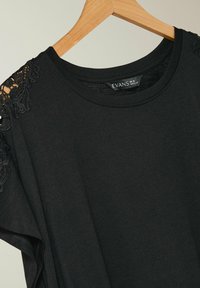T-shirt nero realizzato in tessuto morbido, con dettagli in pizzo sulle spalle e scollatura rotonda. Etichetta visibile sul collo.