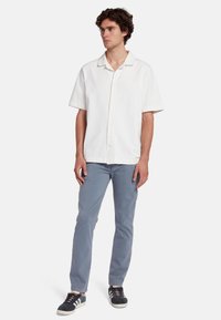 Korte mouwen witte overhemd gemaakt van een lichte stof, gecombineerd met lichtblauwe broek en zwarte sneakers met witte accenten.